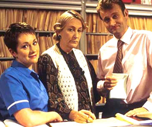 My Hero. Image shows from L to R: Janet Dawkins (Emily Joyce), Mrs Raven (Geraldine McNulty), Dr Piers Crispin (Hugh Dennis). Copyright: Big Bear Films