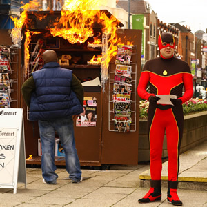 No Heroics. Image shows from L to R: Newspaper Vendor (Delroy Atkinson), Alex, aka The Hotness (Nicholas Burns). Copyright: Tiger Aspect Productions