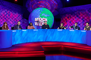Mock The Week. Image shows from L to R: Angela Barnes, Hugh Dennis, Ahir Shah, Dara O Briain, Maisie Adam, Rhys James, Jen Brister