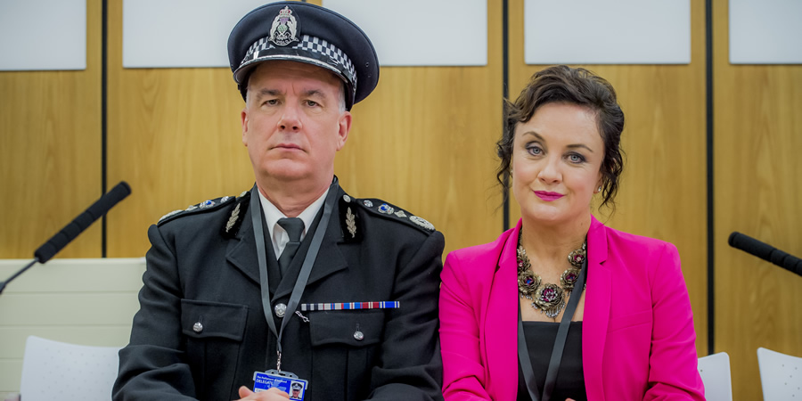 Scot Squad. Image shows from L to R: Chief Commissioner Cameron Miekelson (Jack Docherty), Barbara Edwards (Lorraine McIntosh). Copyright: The Comedy Unit