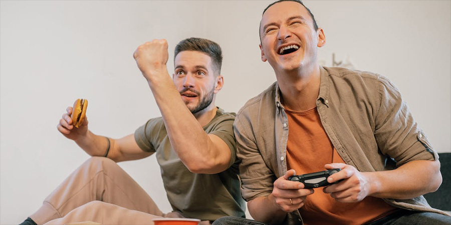 A pair of friends laughing and playing a video game with food