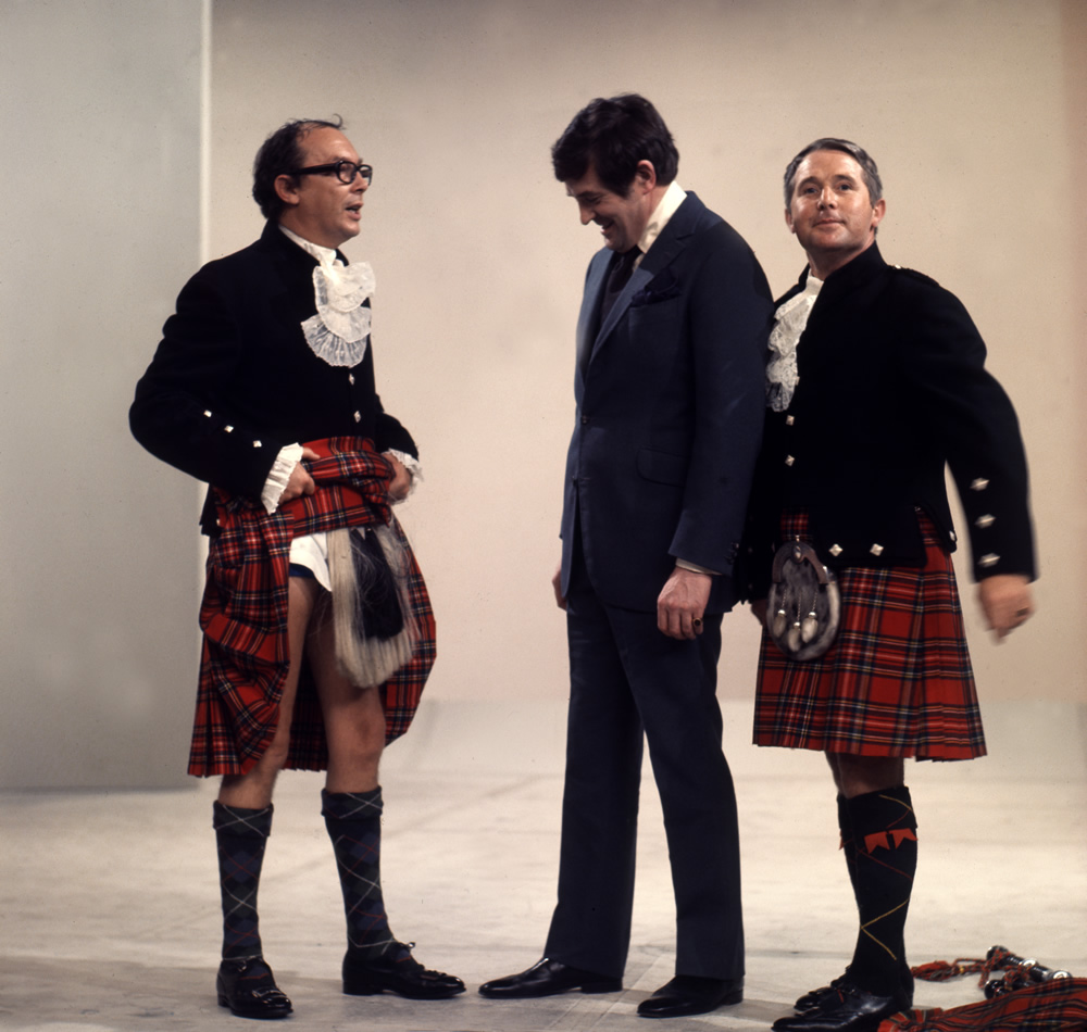 Eric Morecambe in kilt showing Derek Nimmo what he's wearing underneath and Ernie Wise in a kilt. Copyright: BBC History