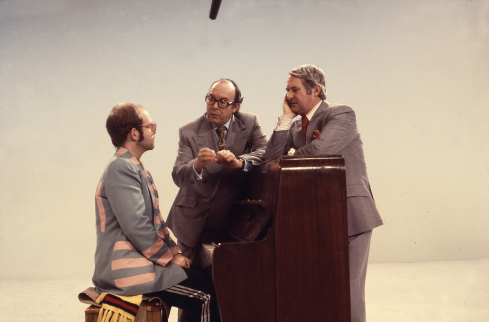 Elton John sat at piano and Eric Morecambe and Ernie Wise, 25/12/1976. Copyright: BBC History