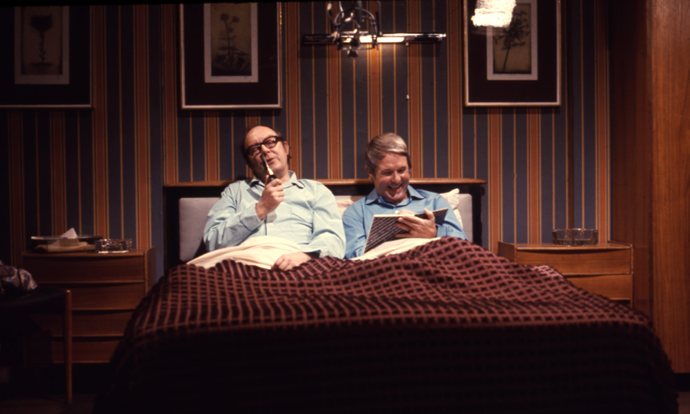 Eric Morecambe and Ernie Wise sharing bed and reading newspapers, 27/09/1974. Image shows from L to R: Eric Morecambe, Ernie Wise. Copyright: BBC History