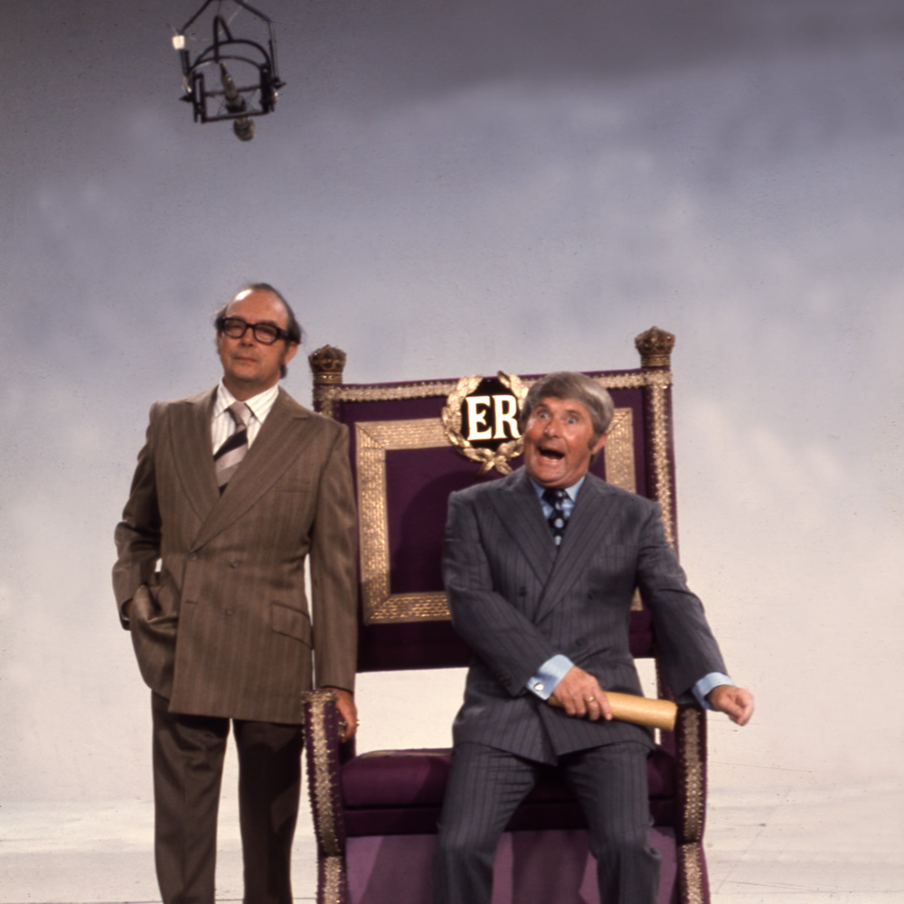 Eric Morecambe standing and Ernie Wise sat on throne, 27/09/1974. Image shows from L to R: Eric Morecambe, Ernie Wise. Copyright: BBC History